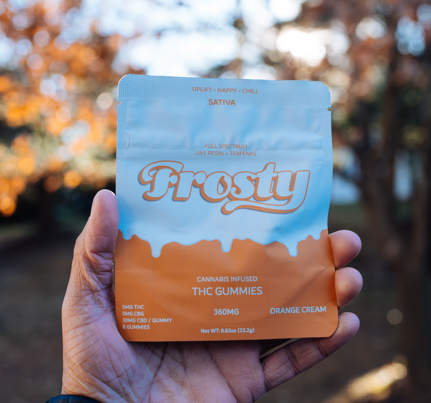 Hand holding Frosty Orange Cream gummies pouch outdoors