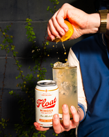 Float Mimosa THC Seltzer can beside a garnished cocktail